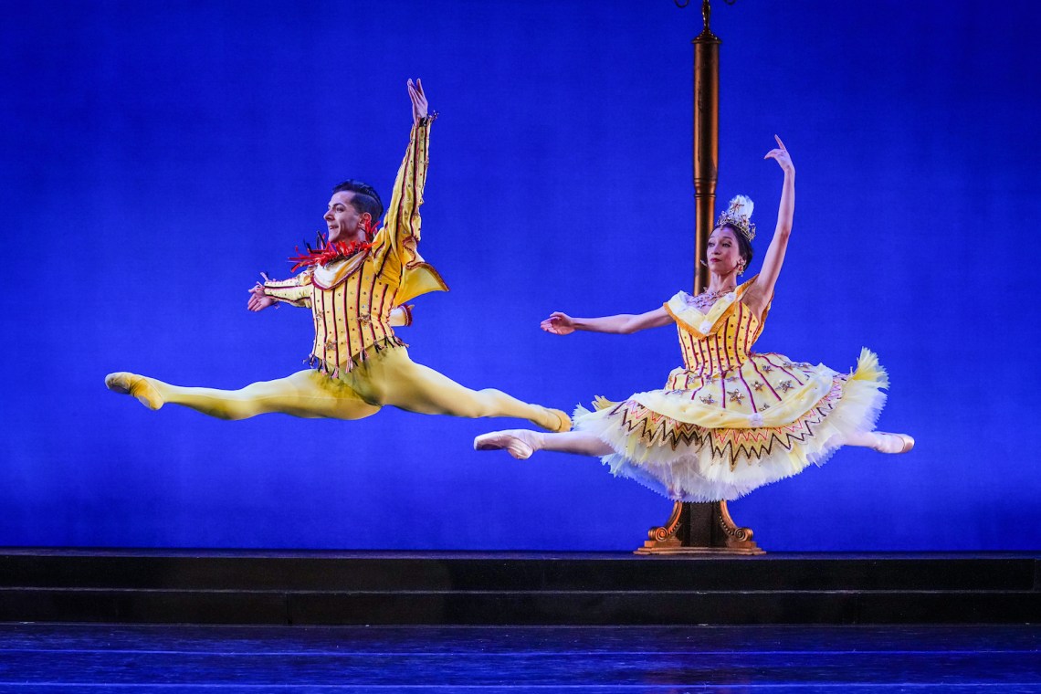 Two ballet dancers in midair, wearing yellow against a blue background