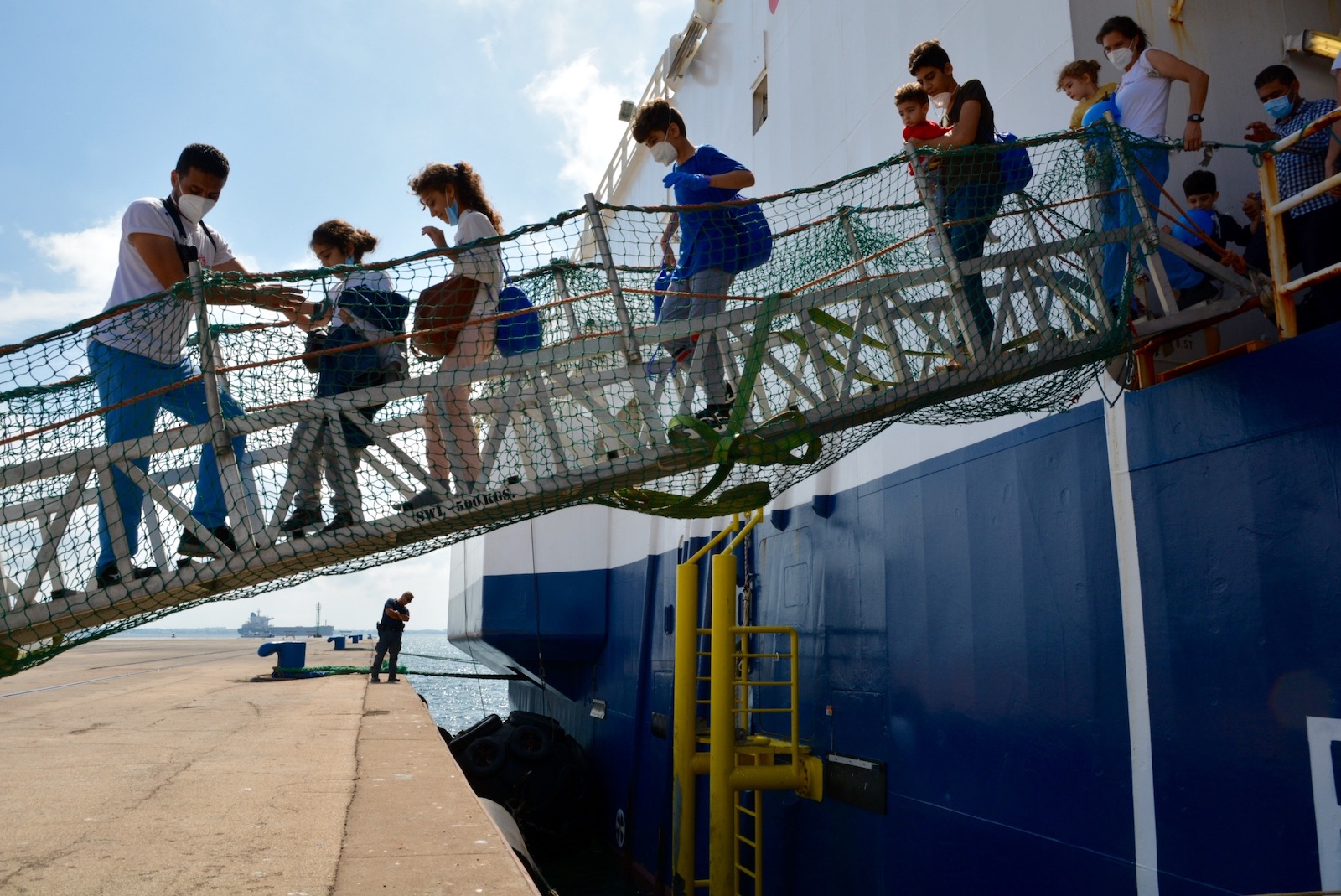 A row of people, including children, descending a plank off a ship