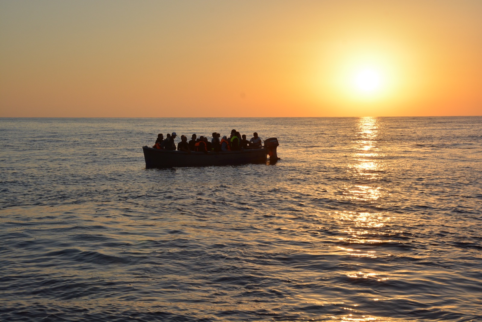 A boat full of people at sea, in silhouette against the setting sun