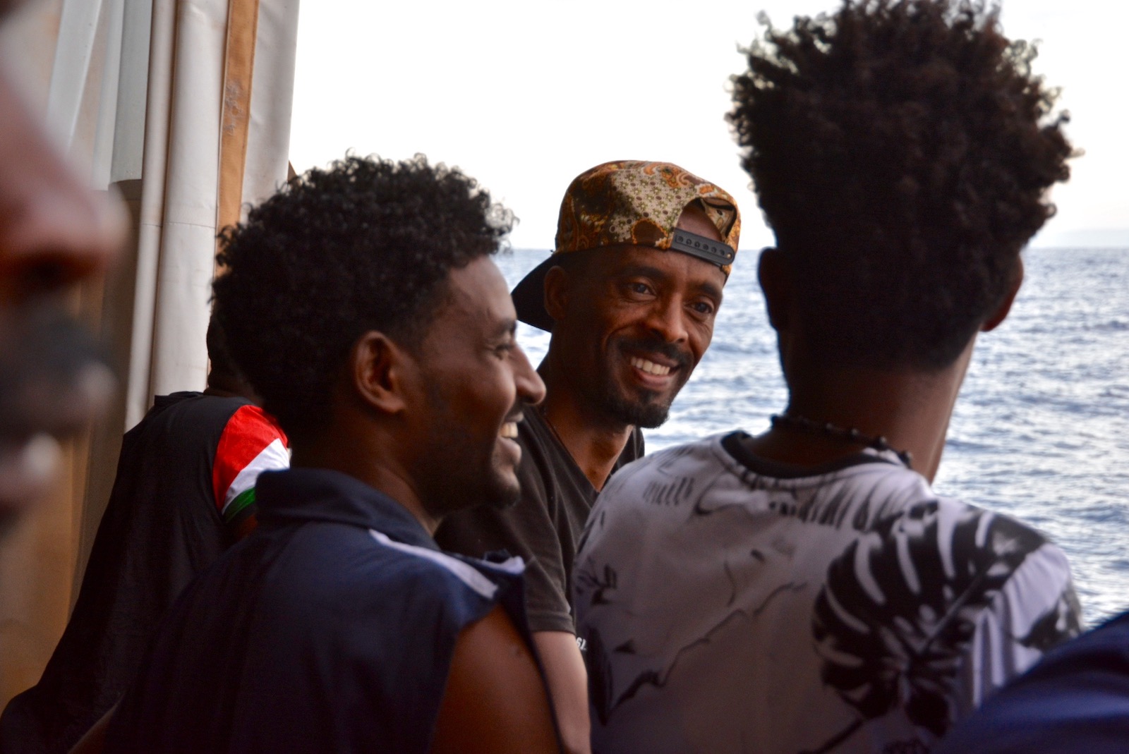 Three men talking and smiling on the deck of a ship