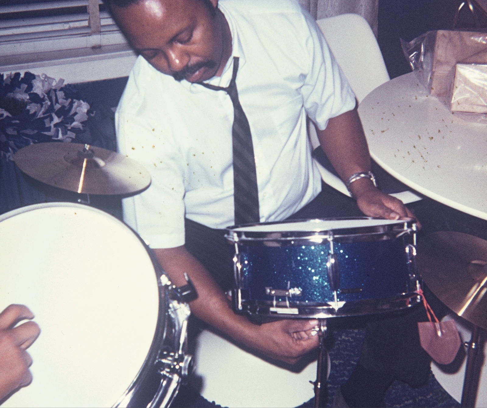 A man behind a drum kit adjusting one of the snare drums