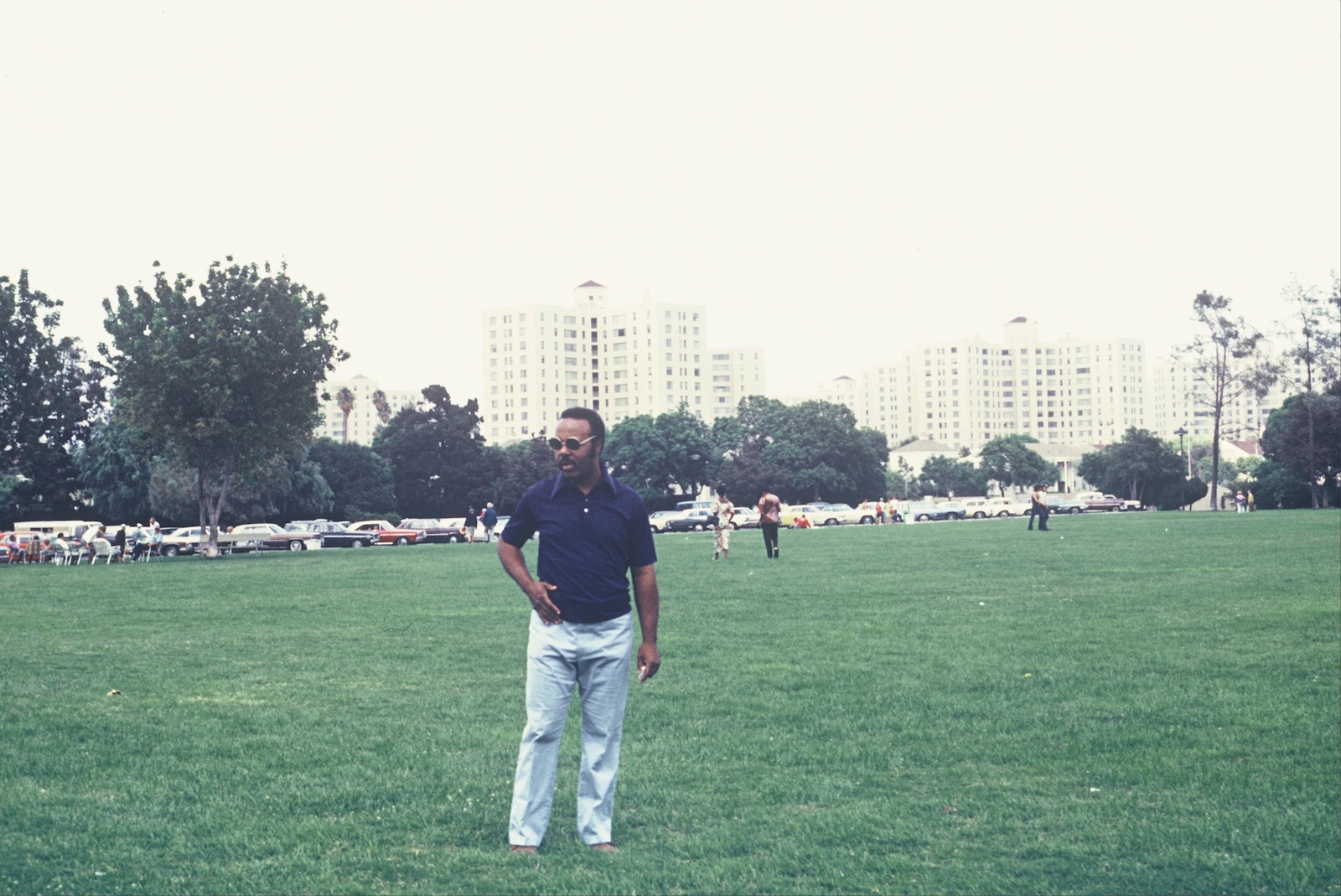 A man standing in a green field with tall buildings in the distance