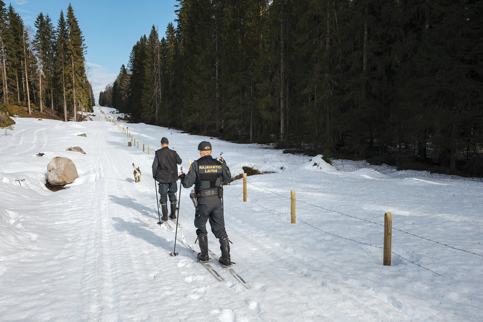 Two guards follow a path on cross country skis with a dog