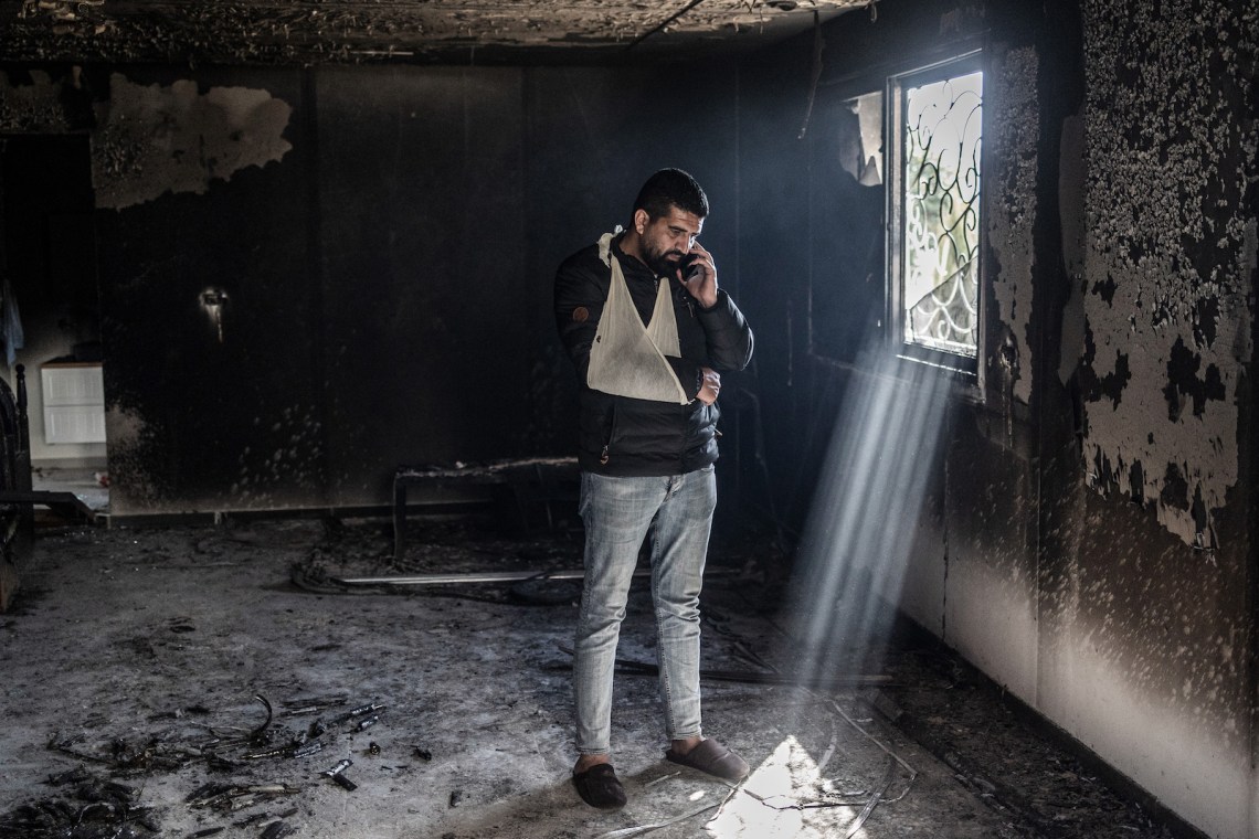 A man standing on a cell phone in a burnt-out building, next to a window through which light streams