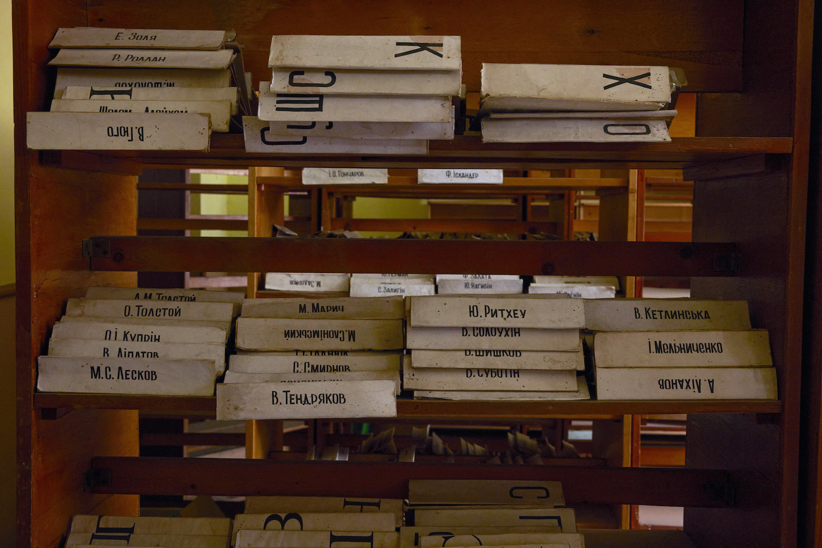 White cardboard subject dividers with labels in Ukrainian are stacked on empty wooden shelves