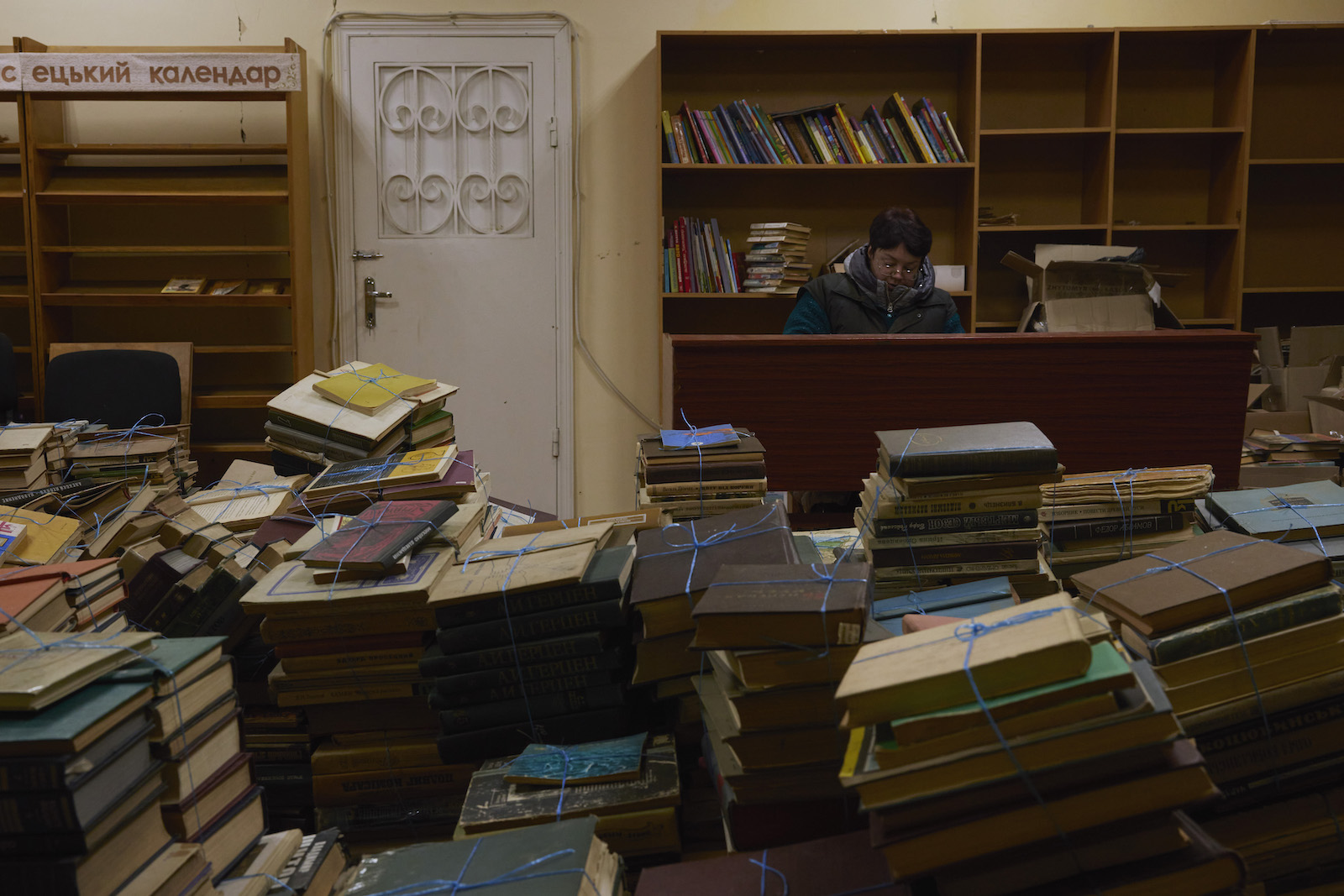 A librarian works at a desk, with piles of bundled library books in the foreground