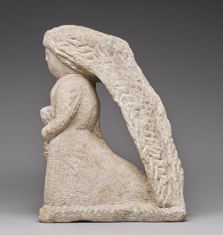 A carved limestone woman in profile with a long veil that arches down to the hem of her dress