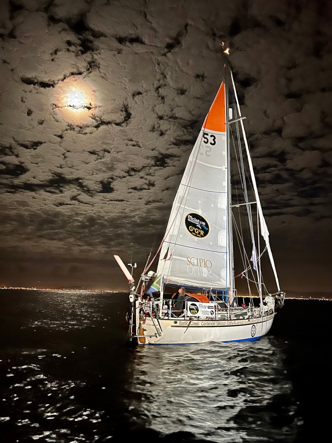 A white sailboat offshore of Cape Town at night under a cloudy full moon