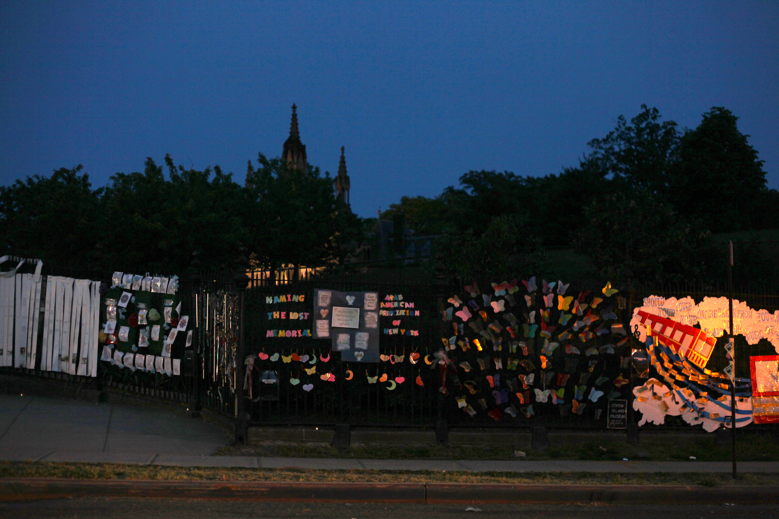 The fence around Green-Wood Cemetery at dusk, with trees and the steeple of the gothic chapel in the background