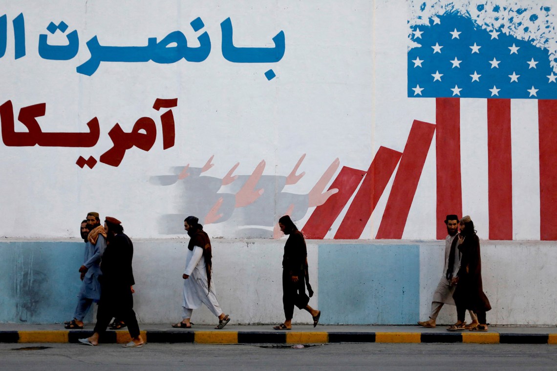 Taliban members walking past a mural on the former US embassy, Kabul