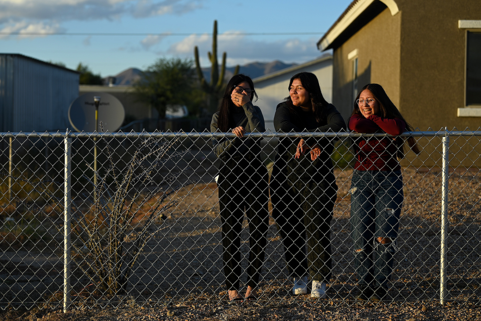 Three young girls standing behind a wire fence