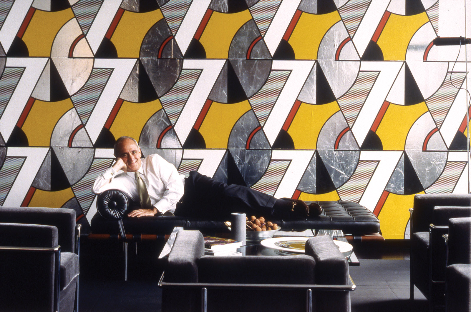 Robert A.M. Stern on a Mies van der Rohe chaise longue in front of Roy Lichtenstein’s vinyl wall covering Modern Banner,